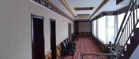 A hallway with a red carpet, wooden doors, and a staircase with metal railings.