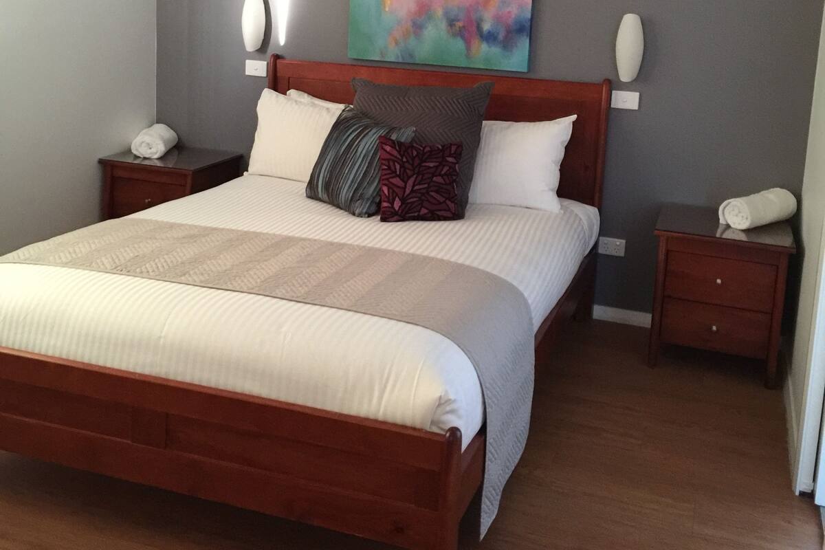 A neatly made bed with a wooden headboard, two bedside tables, and a colorful abstract painting on the wall.