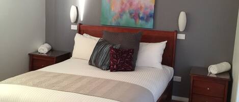 A neatly made bed with a wooden headboard, two bedside tables, and a colorful abstract painting on the wall.