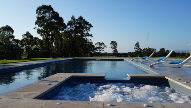 Een zwembad met een jacuzzi, ligbedden en een heldere lucht.