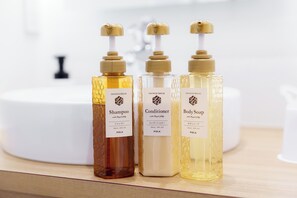 Three bottles of shower products on a countertop with a white sink in the background. - Sakura Garden Hotel (Osaka)
