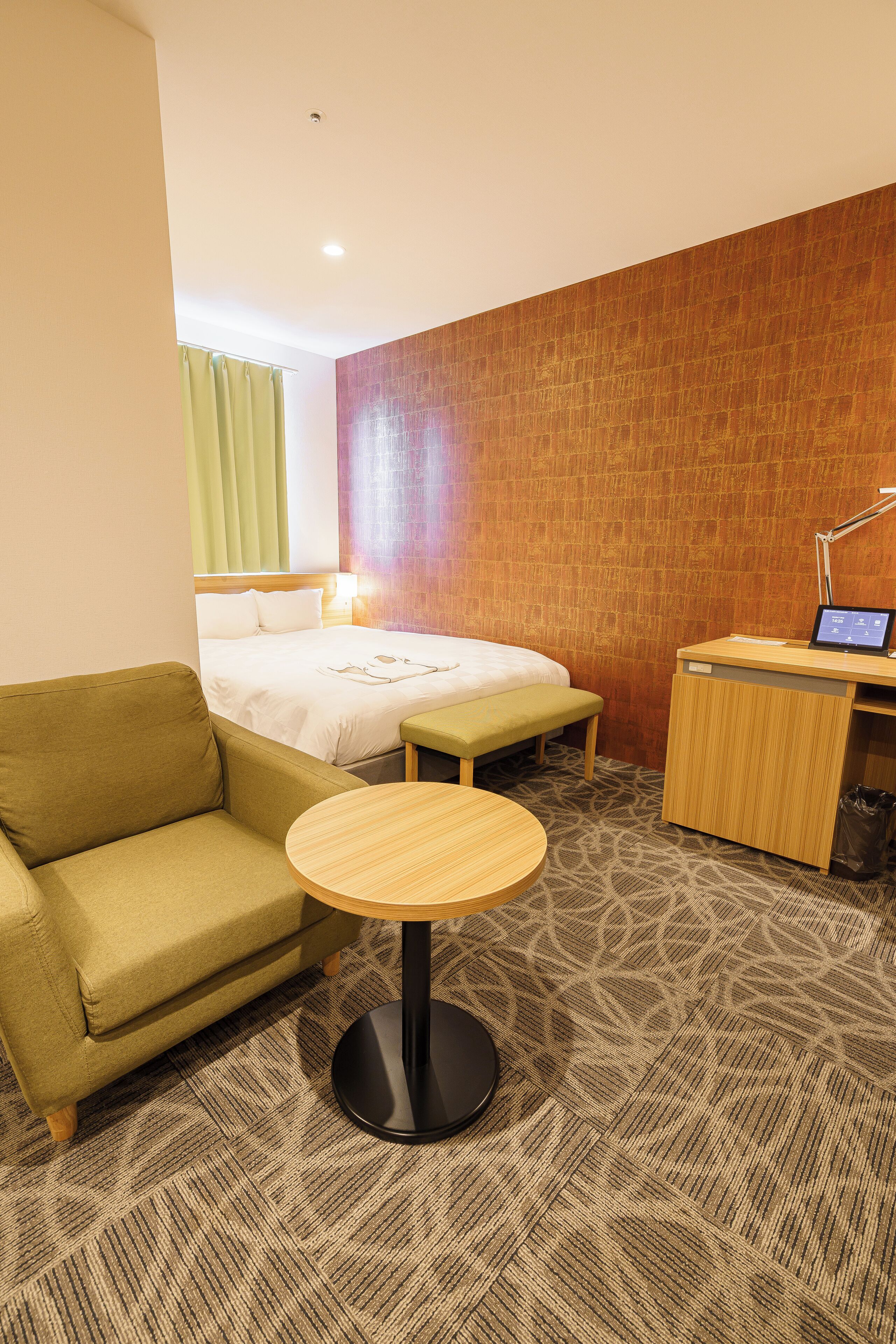 A hotel room with a bed, a sofa, a small table, and a desk with a computer.