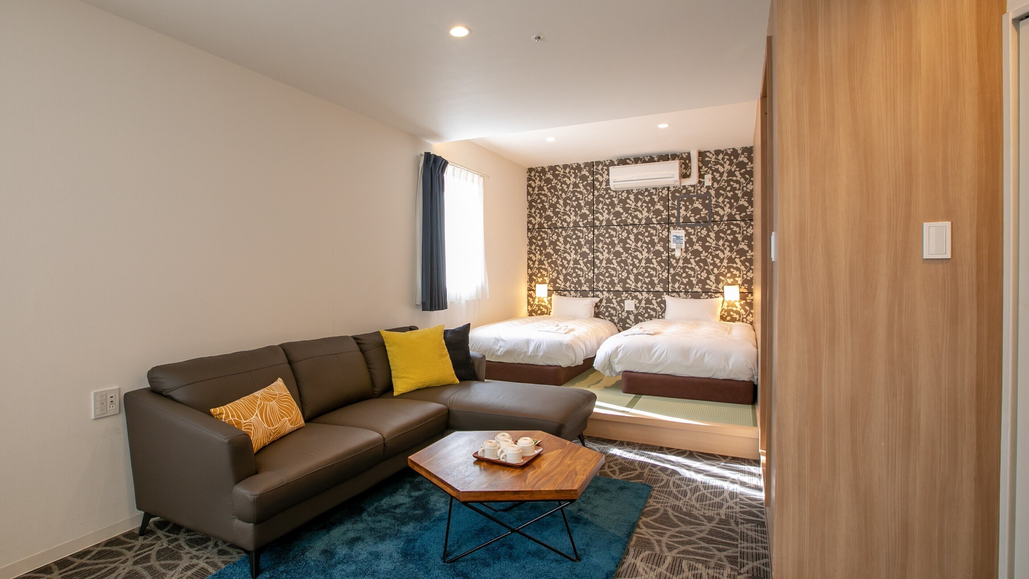 A hotel room with a sofa, two beds, a wooden coffee table, and a patterned carpet.