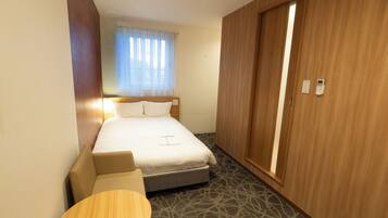 A hotel room with a bed, a small table, and a wardrobe.