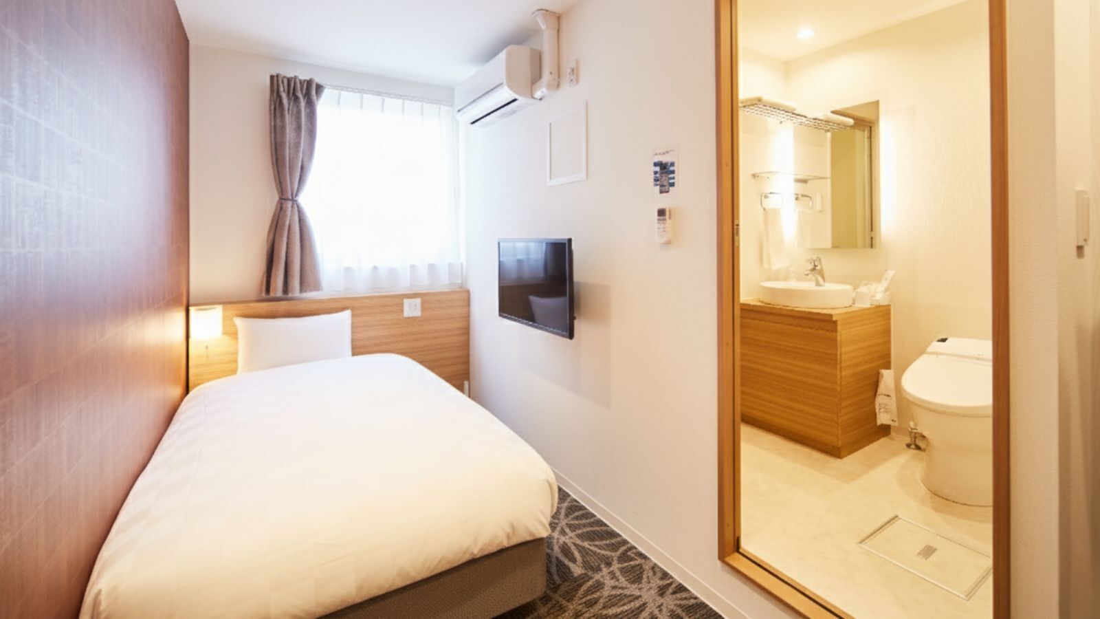A hotel room with a bed, a TV, a bathroom with a sink and toilet, and a window with curtains.
