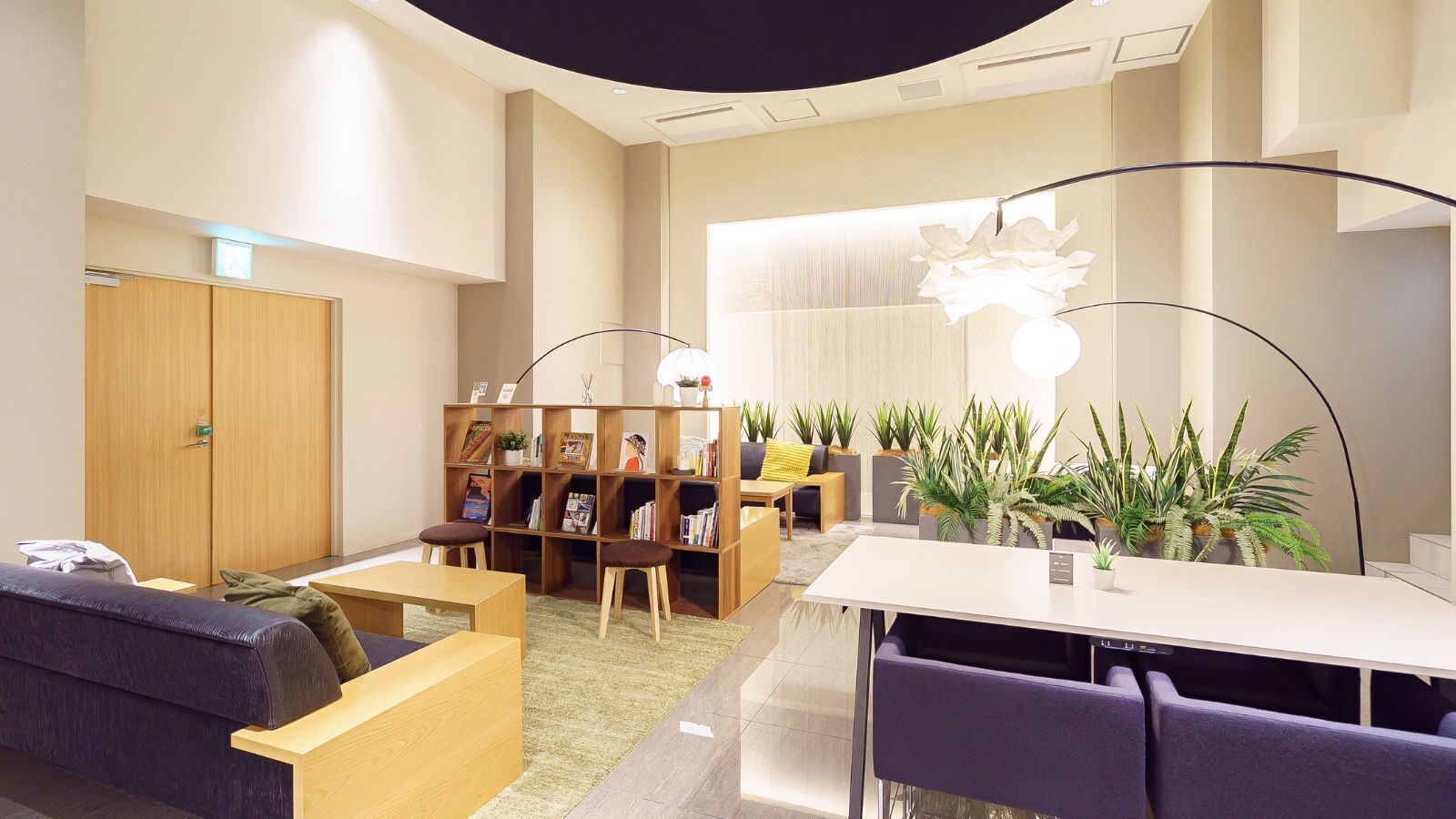 A modern lounge area with a sofa, chairs, a table, a bookshelf, and potted plants.
