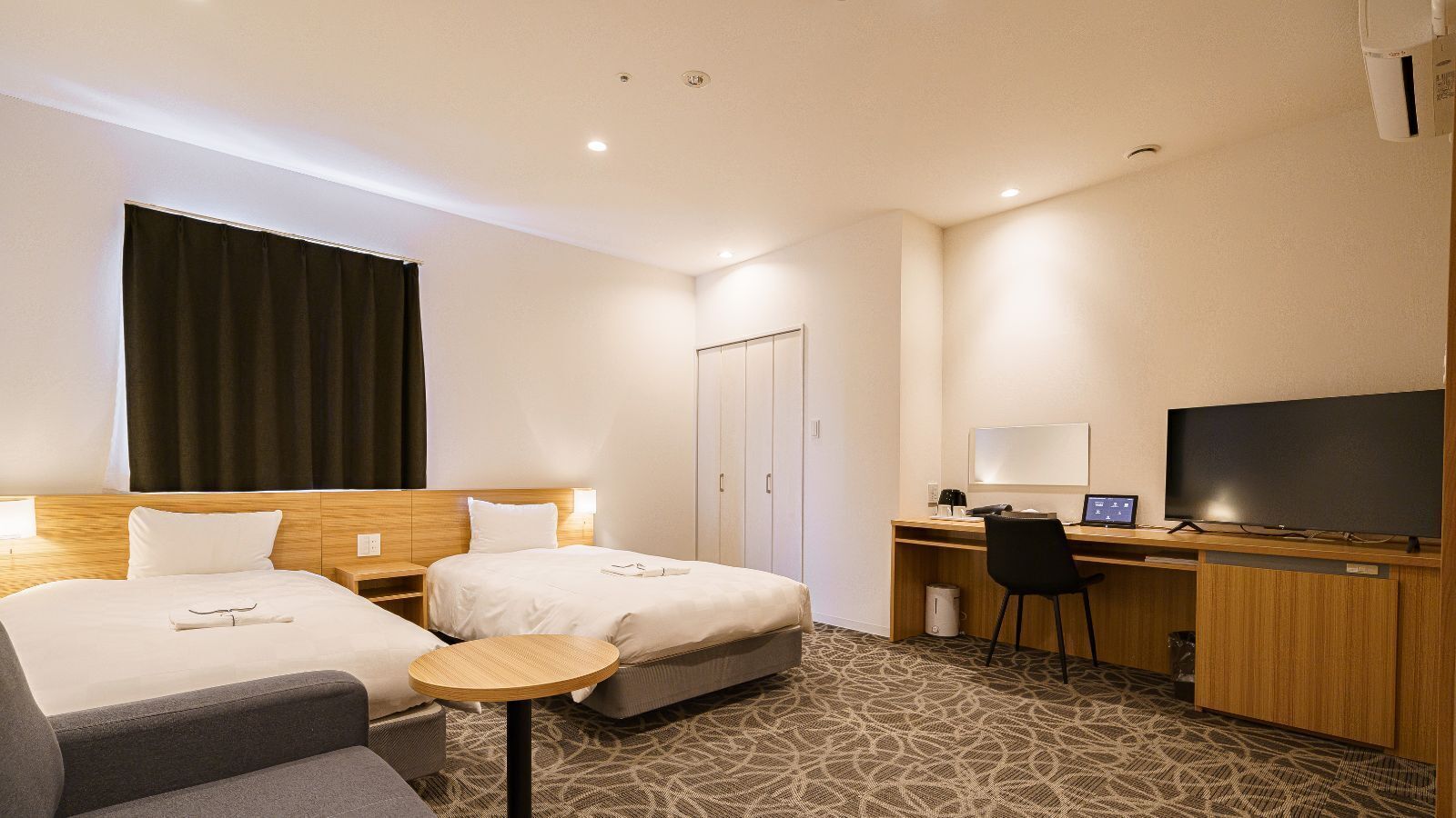 A hotel room with two beds, a desk with a computer, a TV, and a small round table.