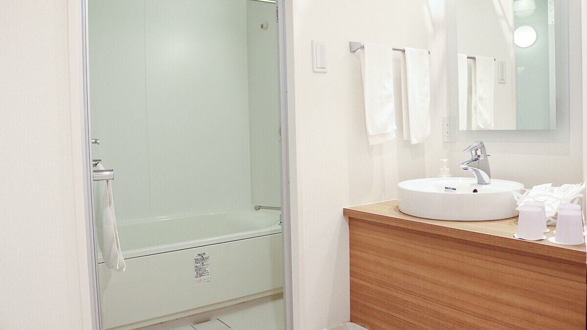 A bathroom with a glass-enclosed shower, a white sink with a mirror, and a wooden vanity.