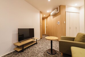 A modern living room with a flat-screen TV, a wooden bench, a round table, and a green sofa. - Sakura Garden Hotel (Osaka)