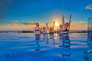 Un grupo de personas en una piscina, con un atardecer al fondo.