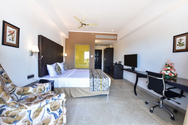 Habitación de hotel con cama, escritorio, silla, televisión y ventilador de techo.