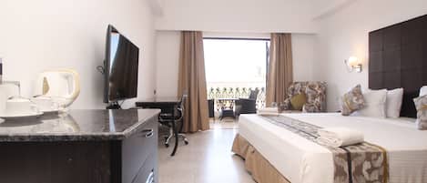 Habitación de hotel con cama, escritorio, silla, televisor y balcón con vistas.