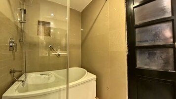 Un baño con ducha envuelta en vidrio, una bañera blanca y una puerta negra.