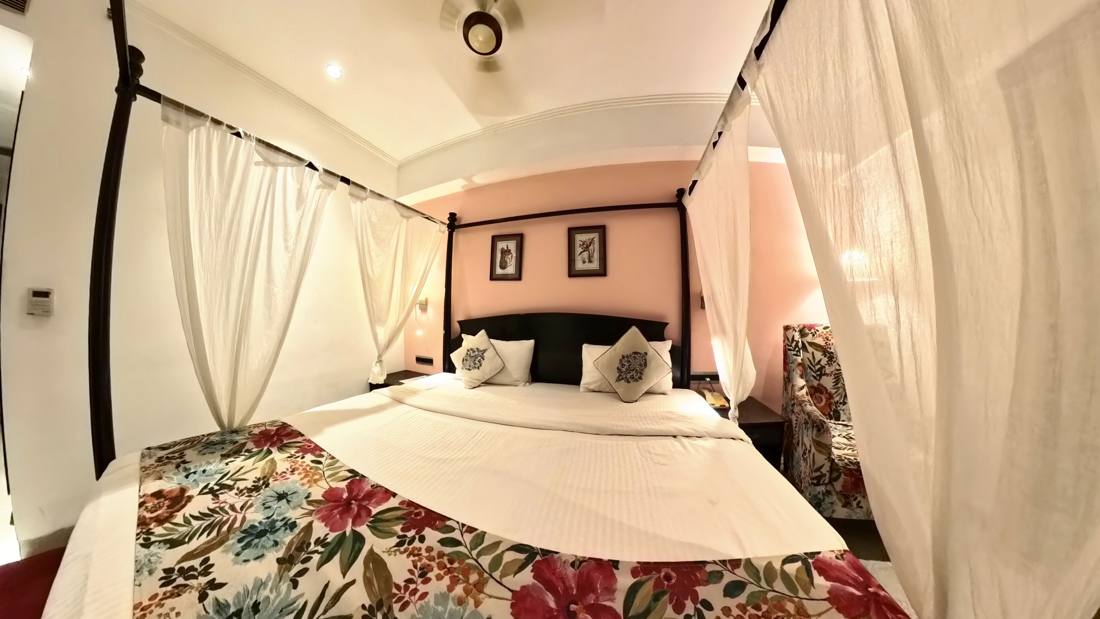 Un dormitorio con cama con dosel, colcha estampada y dos cuadros colgados en la pared.