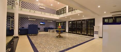A spacious lobby with a patterned floor, a central table with a vase, and a television on the wall.