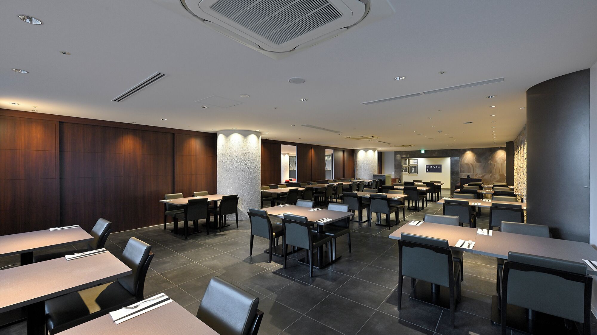 Un'area pranzo moderna con diversi tavoli e sedie, illuminazione a incasso e una parete decorativa in pietra.