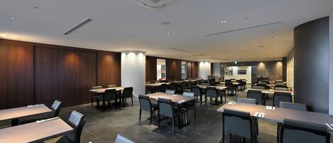 Un'area pranzo moderna con diversi tavoli e sedie, illuminazione a incasso e una parete decorativa in pietra.