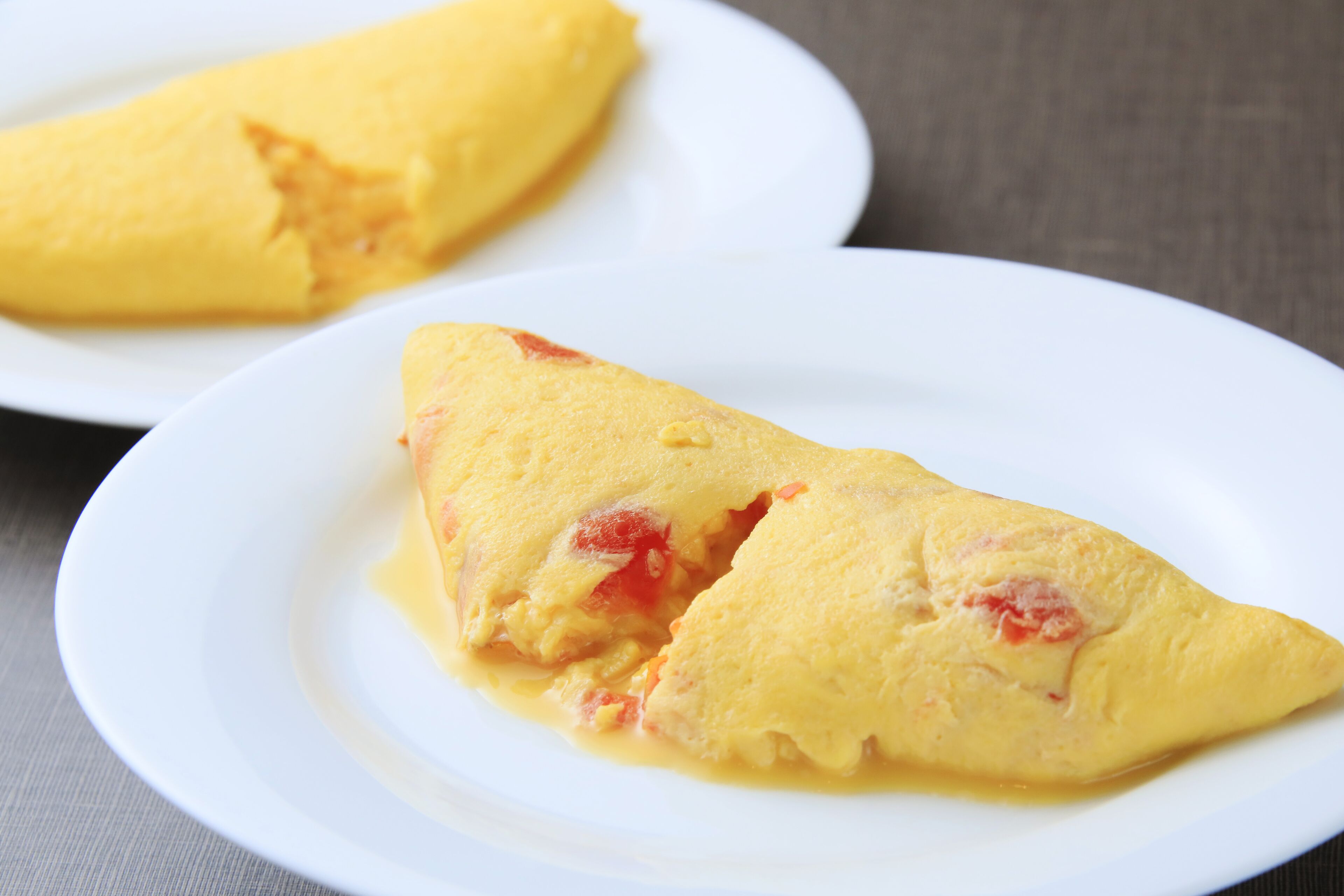 Two white plates with a folded omelette on one of them.