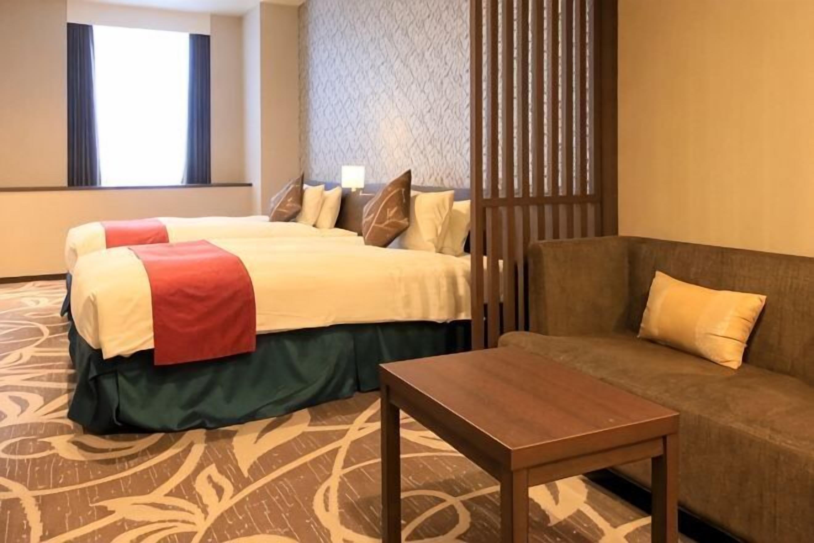 Een hotelkamer met een tweepersoonsbed, een bank, een klein tafeltje en een kamerbreed tapijt met een patroon.