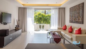 A modern living room with a flat-screen TV, a sofa with red cushions, a coffee table, and a large window with curtains. - The Pearl of Naithon (Sa Khu)