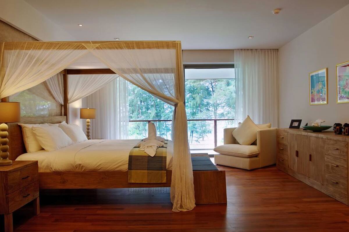 A bedroom with a four-poster bed, a sitting area with a sofa, and a wooden cabinet.