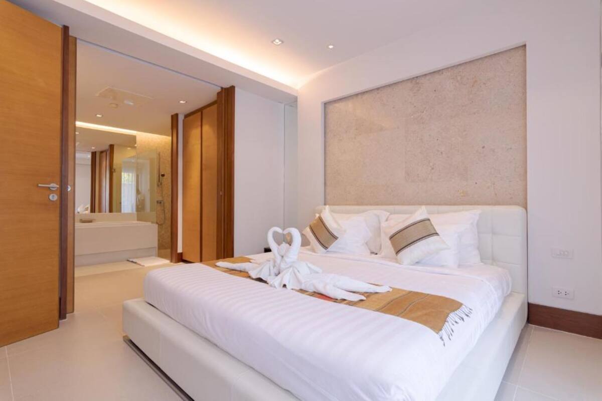 A modern hotel room with a large bed, a wooden door, and a bathroom visible in the background.