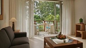 A modern hotel room with a sofa, a wooden coffee table with fruit, a dining area with a table and chairs, and a balcony with a view of trees. - The Pearl of Naithon (Sa Khu)