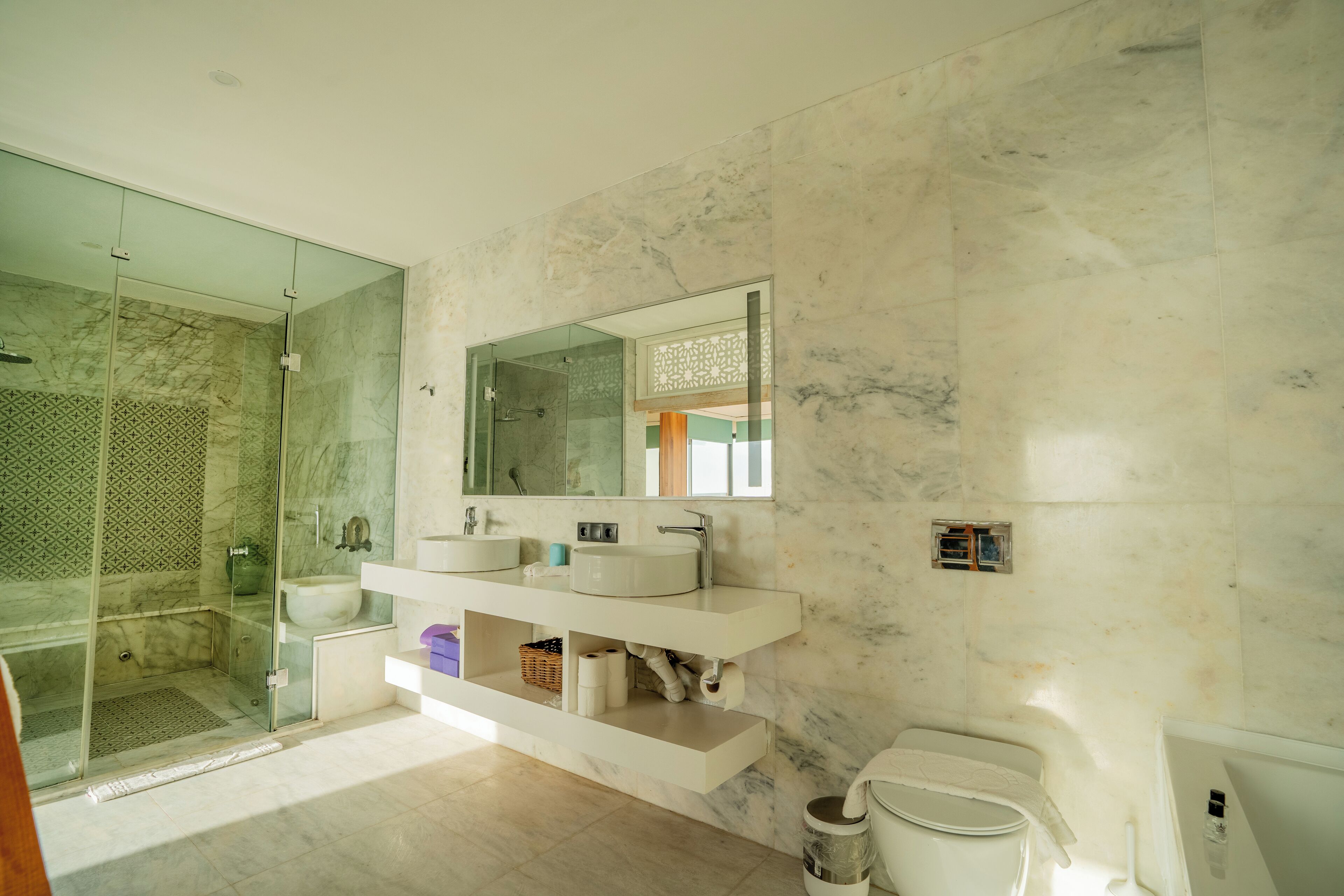 A modern bathroom with a glass-enclosed shower, a marble-tiled wall, a white sink vanity, and a toilet.