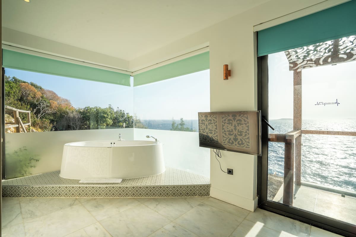 Un baño moderno con una bañera independiente, un televisor y un amplio ventanal con vistas panorámicas.