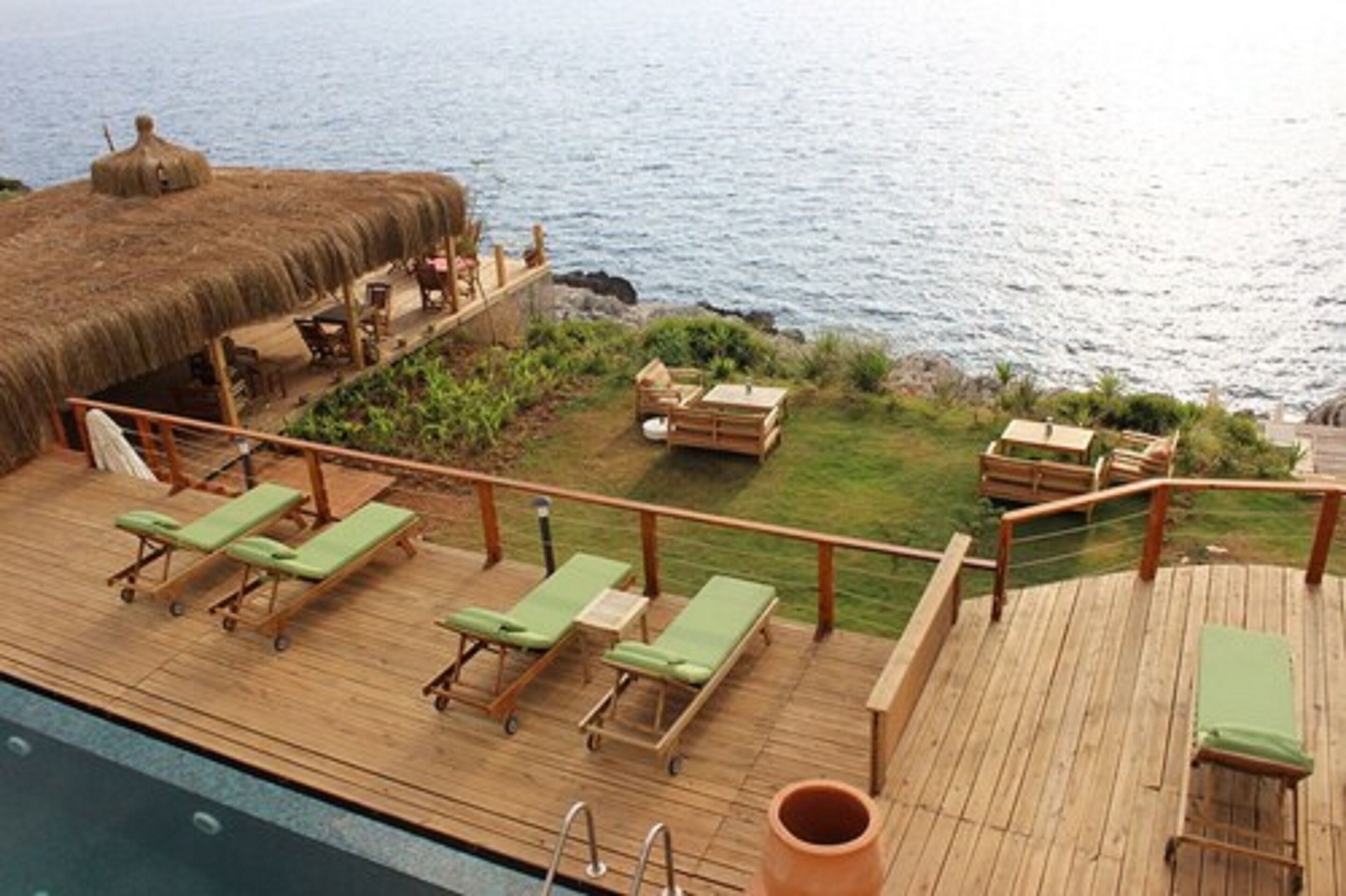 A wooden deck with lounge chairs and a thatched-roof structure overlooking the sea.