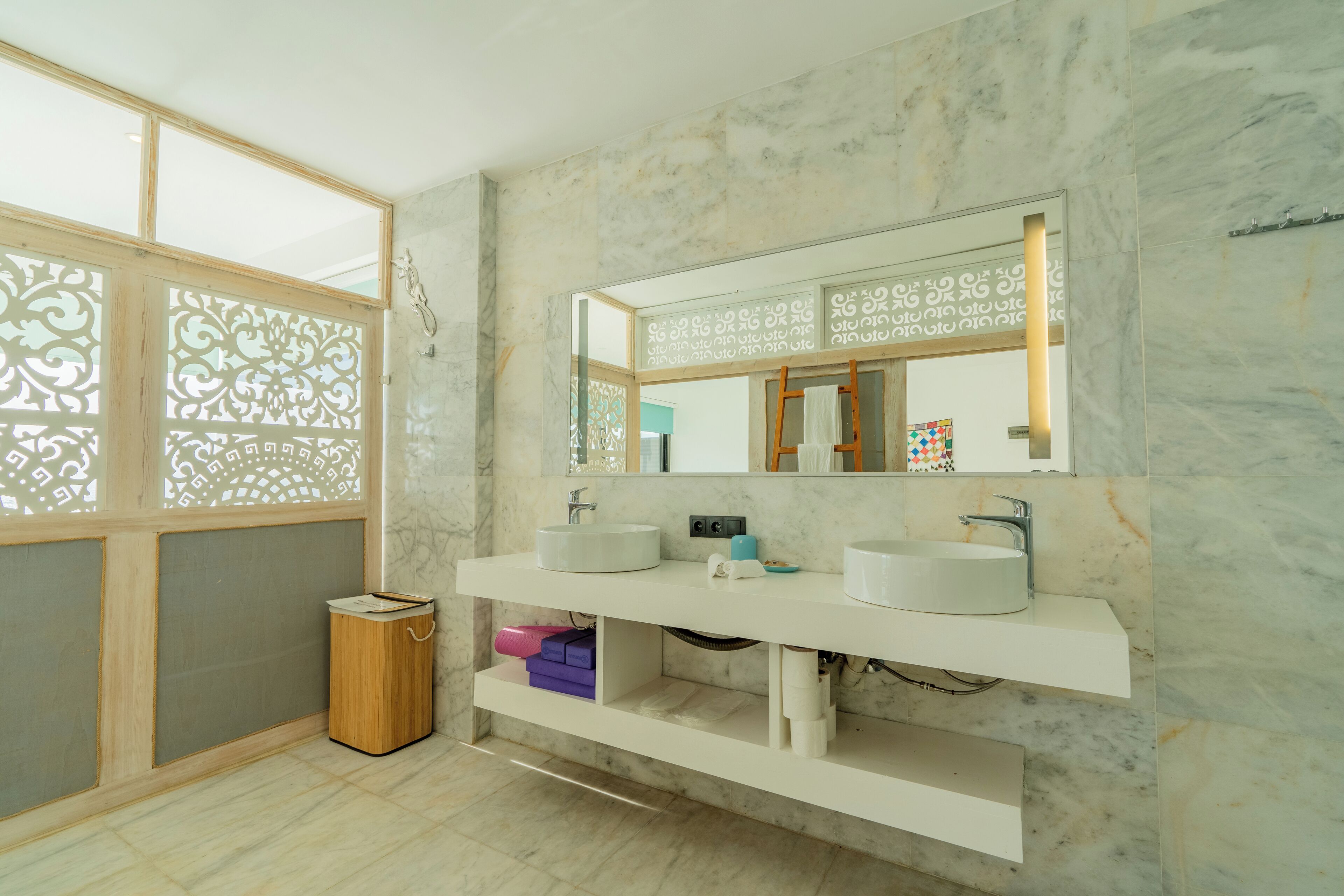 A modern bathroom with two sinks, a mirror, and a wooden trash bin.