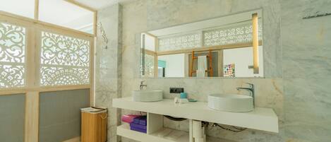 A modern bathroom with two sinks, a mirror, and a wooden trash bin.