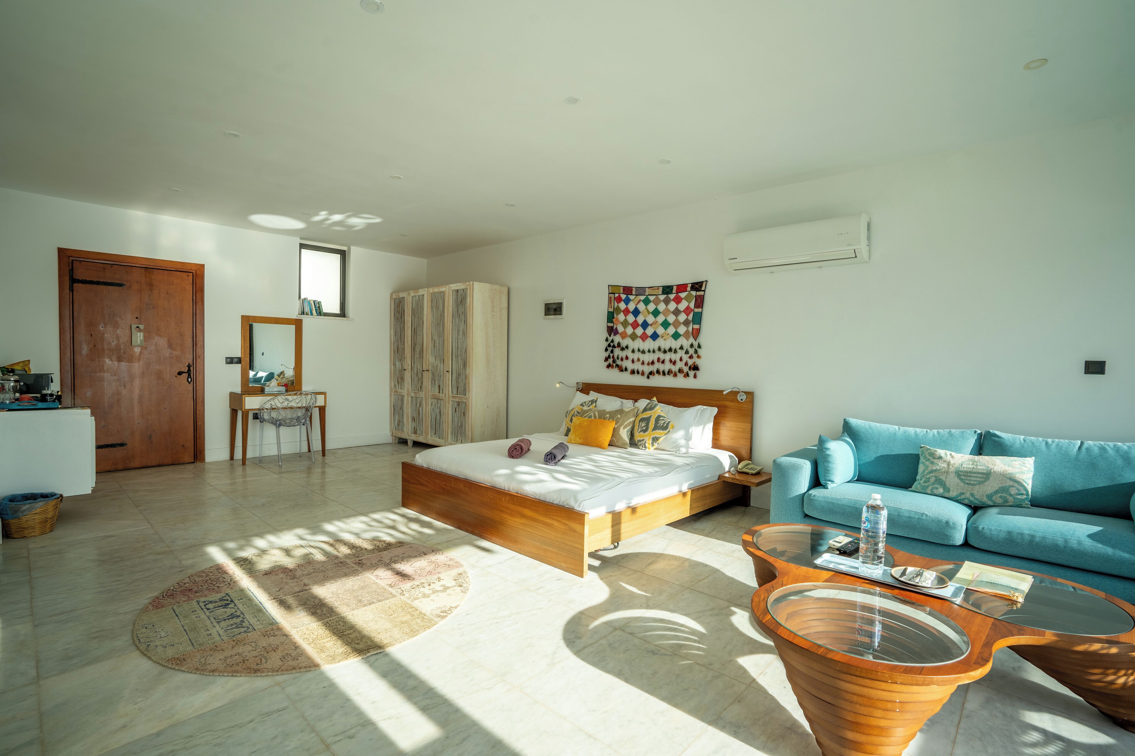 A modern bedroom with a bed, a blue sofa, a wooden coffee table, and a large mirror.