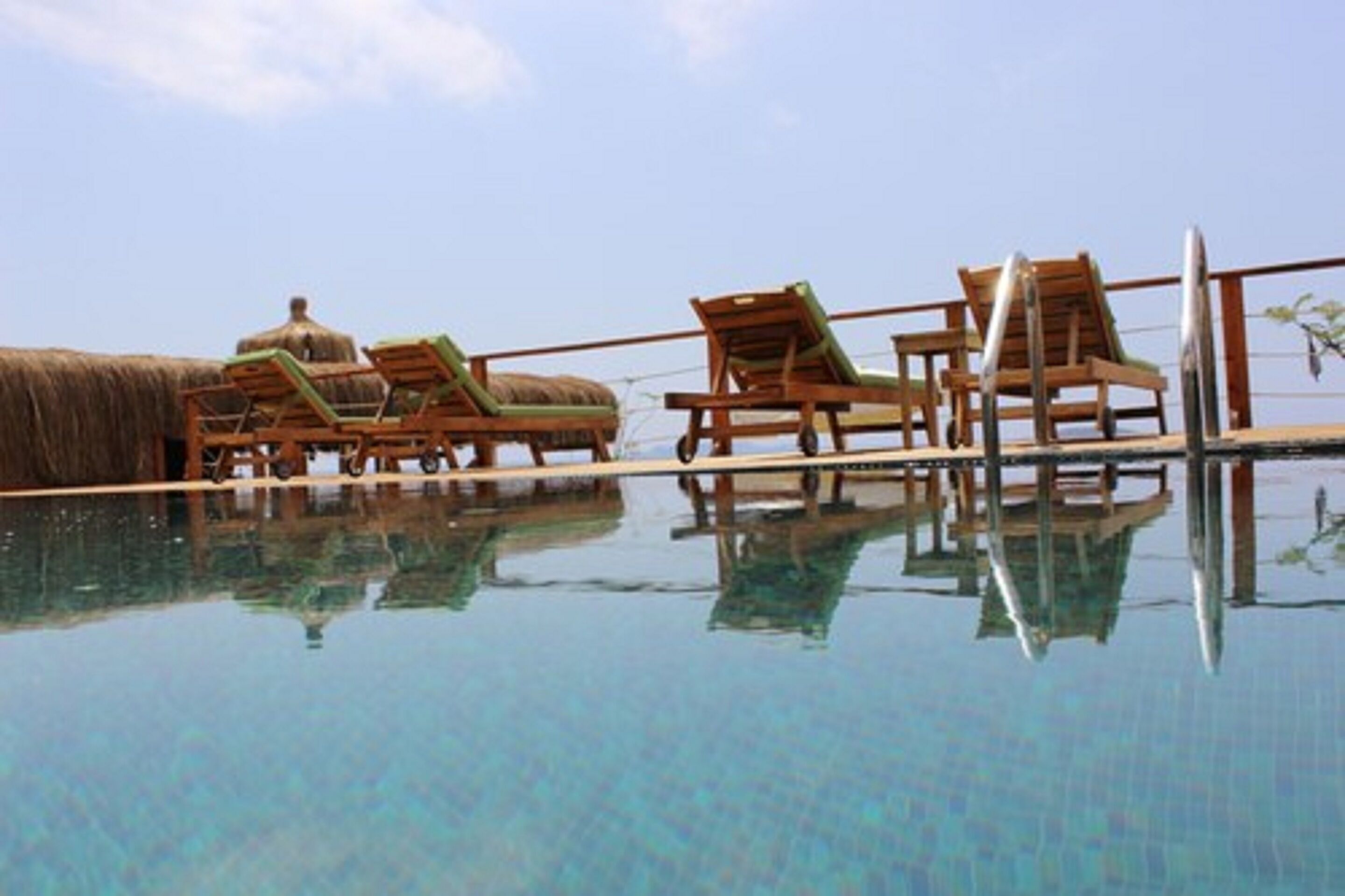 Una piscina infinita con sillones de madera y una estructura de paja.