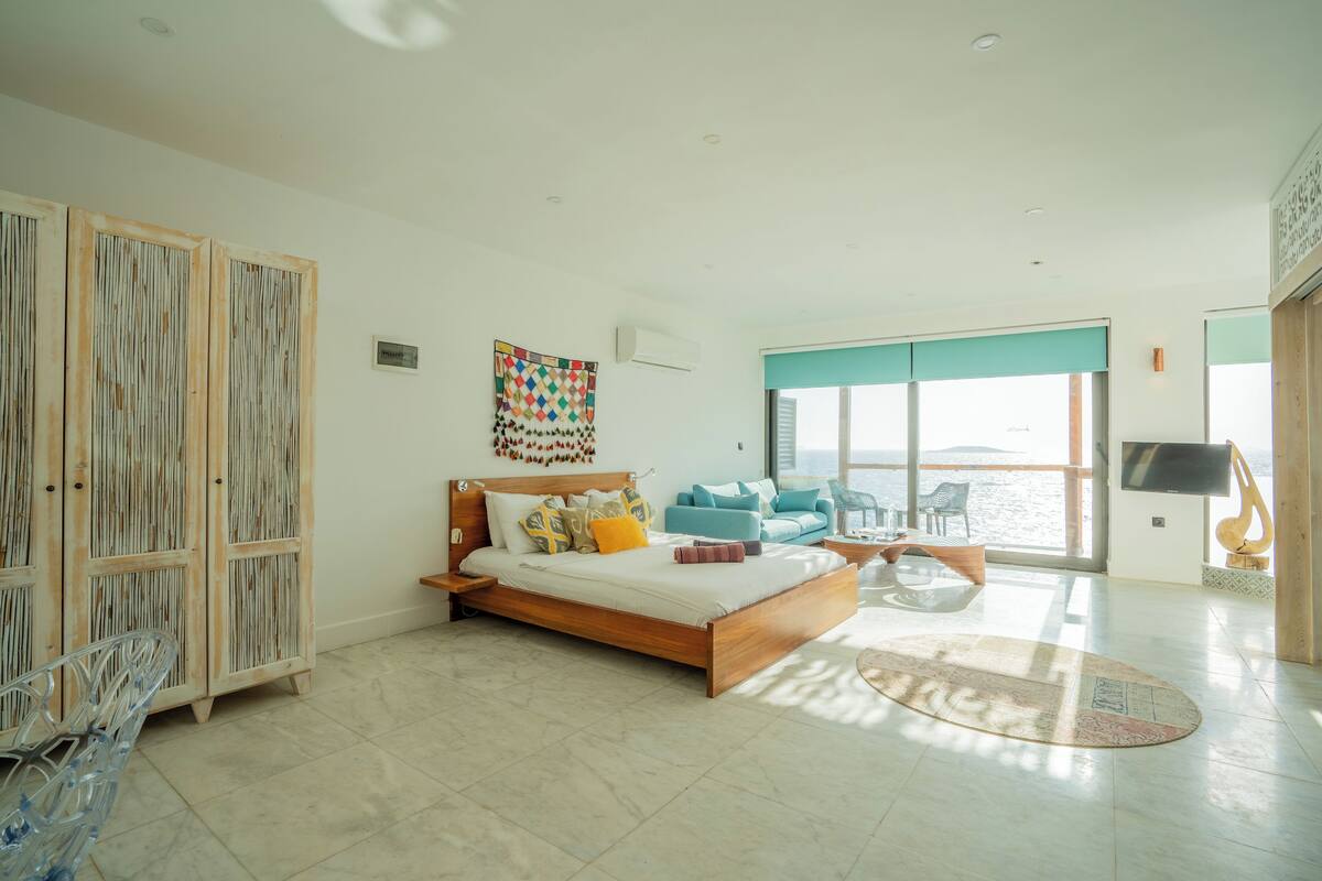 Un dormitorio amplio con una cama grande, vista al mar y un televisor.