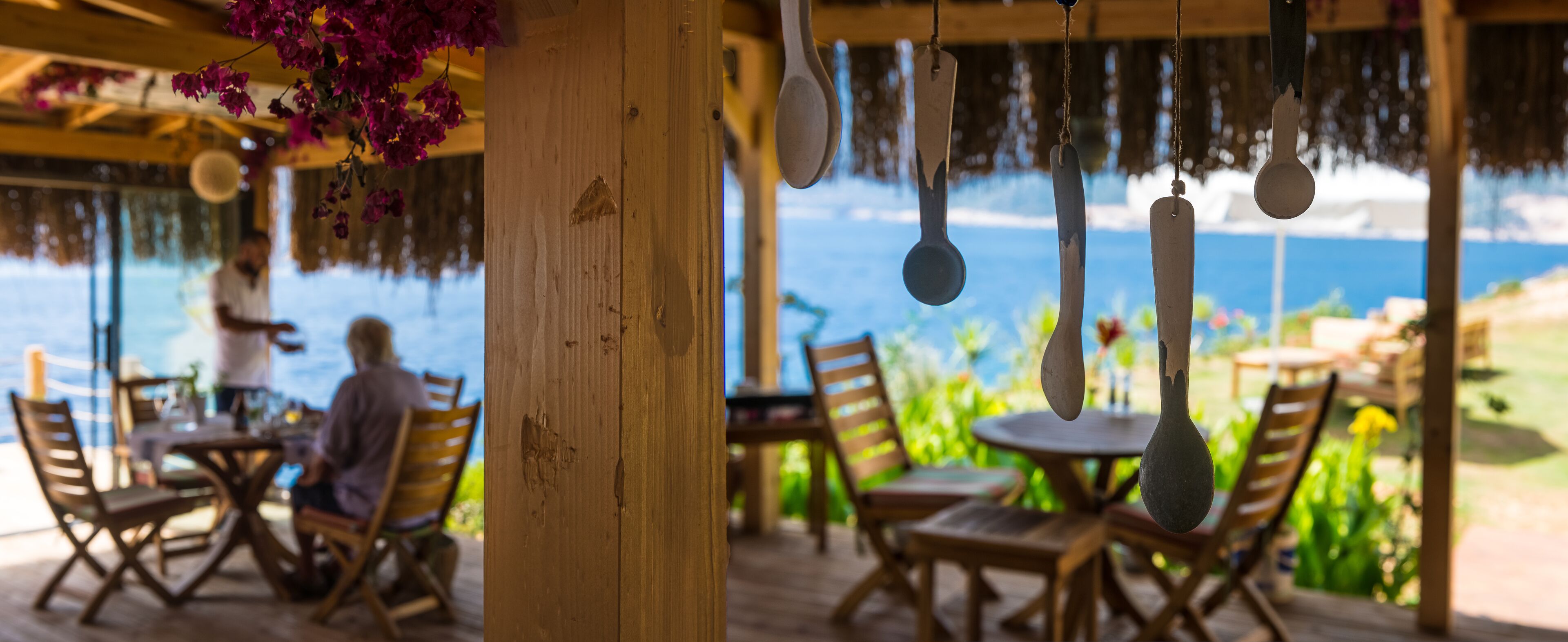 A wooden deck with tables and chairs, overlooking a body of water.