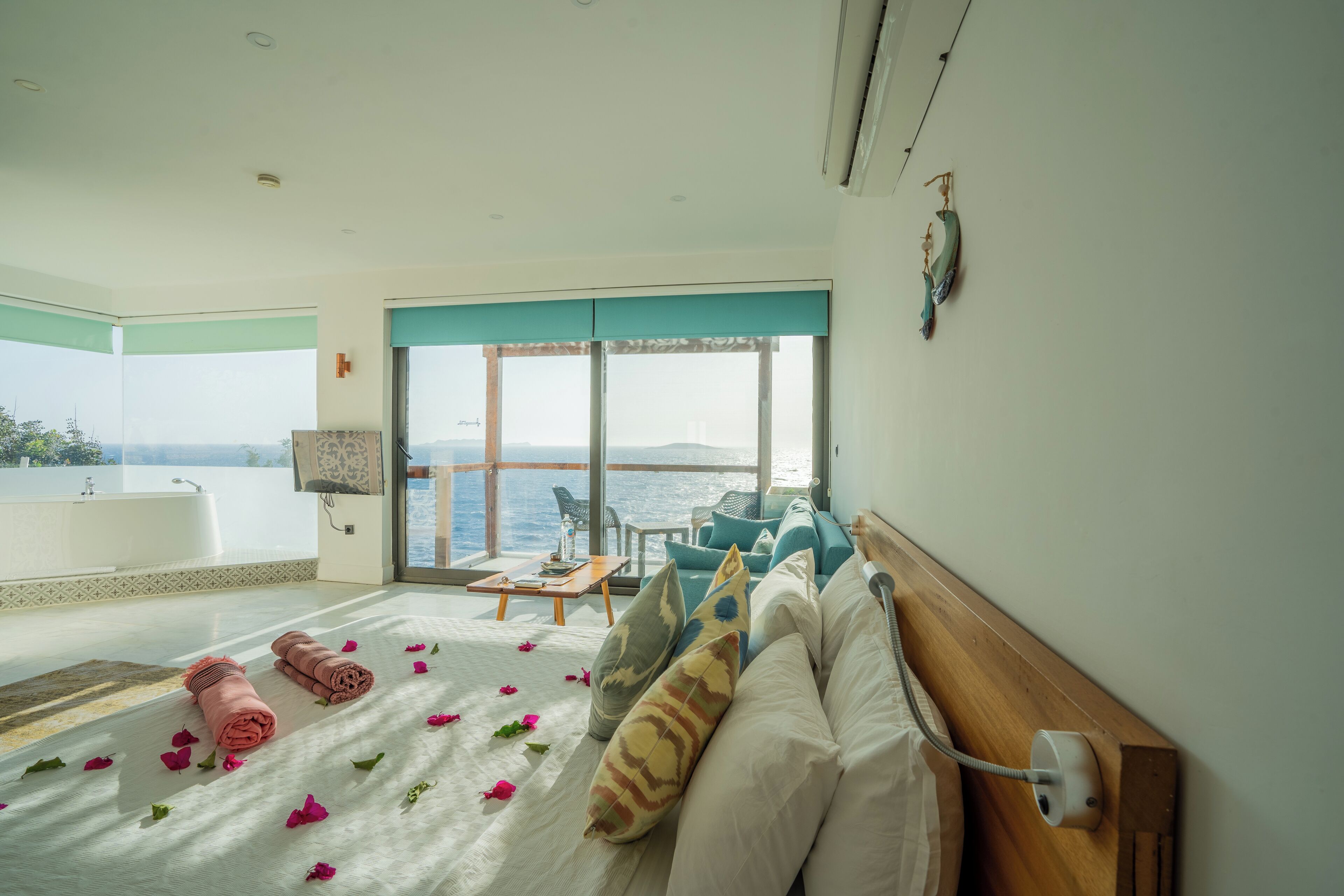 A spacious bedroom with a large bed, a view of the sea, a bathtub, and a seating area with a table and chairs.