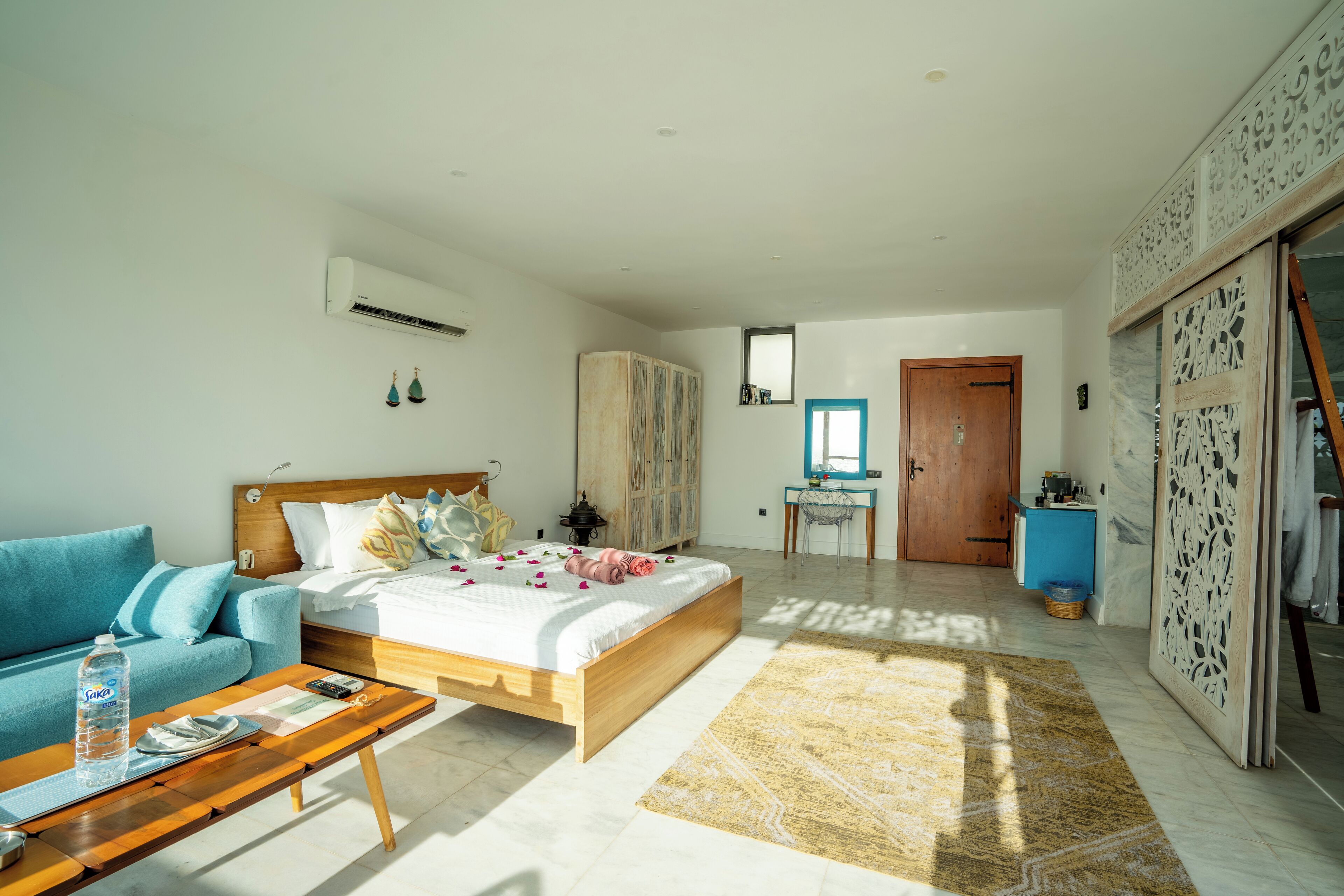 A modern bedroom with a wooden bed, a blue sofa, a wooden coffee table, and a small desk with a chair.