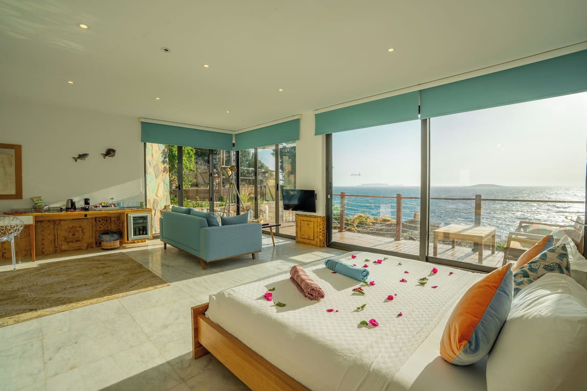 Un dormitorio moderno con una cama grande, un sofá, un televisor y un balcón con vistas al mar.