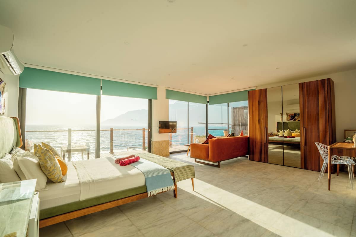 Un dormitorio amplio con una cama grande, una zona de estar con vistas al mar y un comedor separado.
