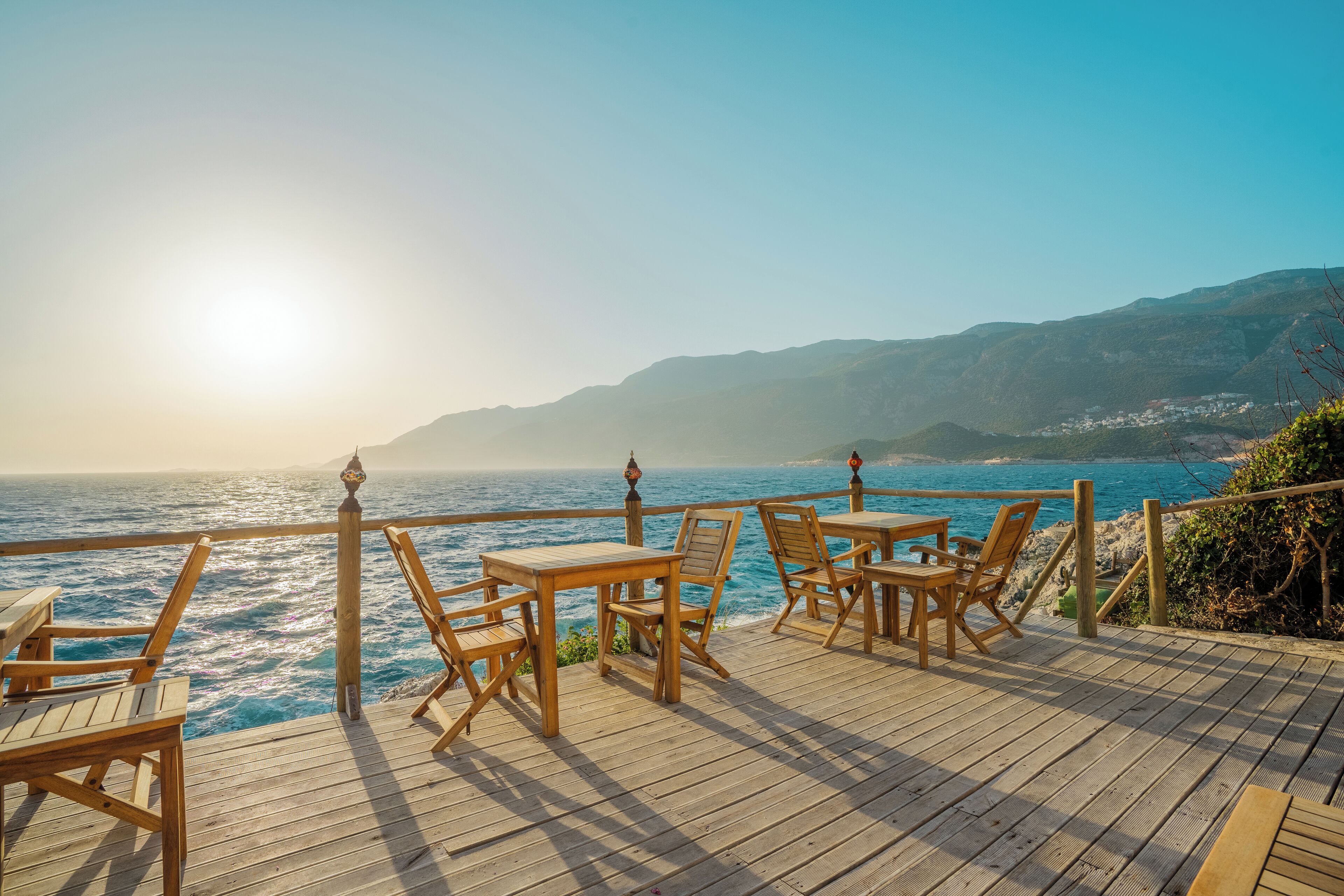 A wooden deck with tables and chairs overlooking a coastal view.