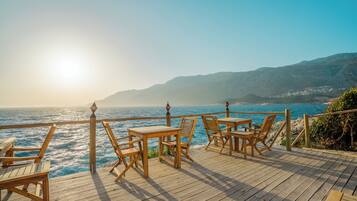 A wooden deck with tables and chairs overlooking a coastal view.