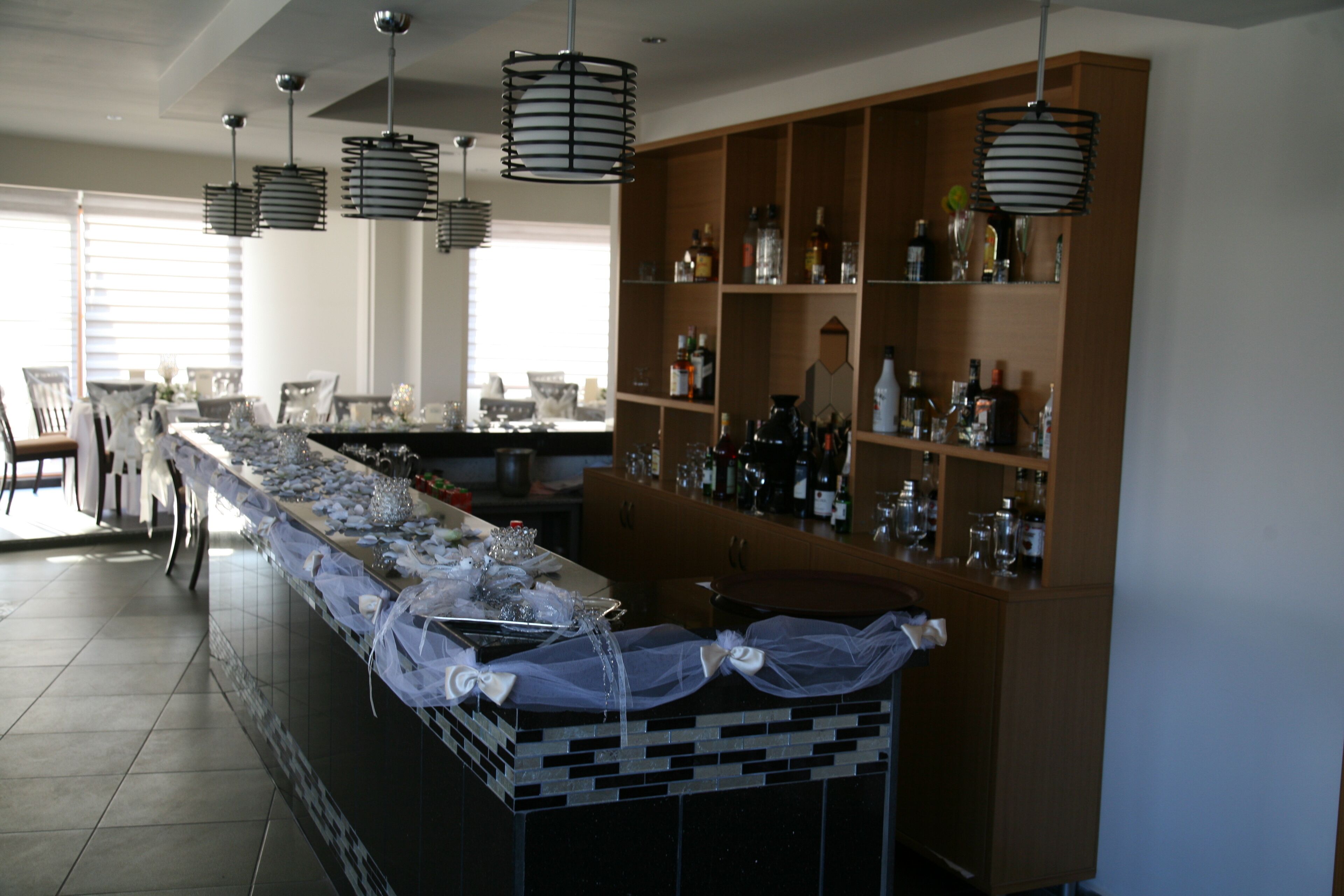 Een bar met een lange toonbank, hangende hanglampen en flessen op de planken.