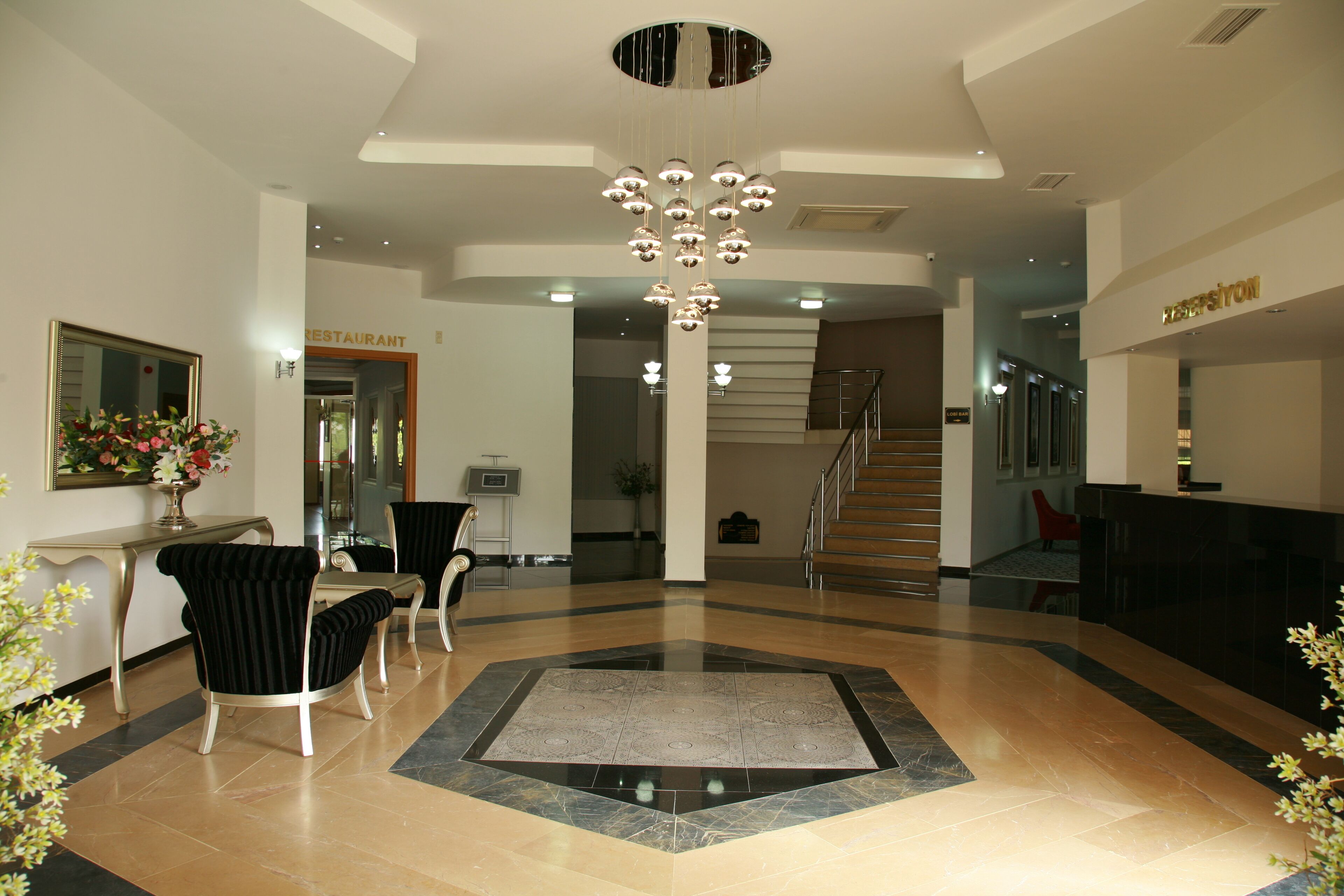 Een hotellobby met een receptiebalie, een trap en een eetgedeelte.