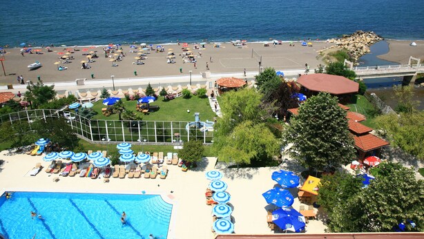 Un complejo turístico en la playa con piscina, tumbonas, sombrillas y vistas al mar.