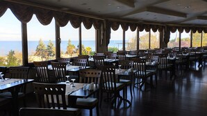 Un amplio comedor con mesas y sillas, ventanas grandes con cortinas, y vista al mar.