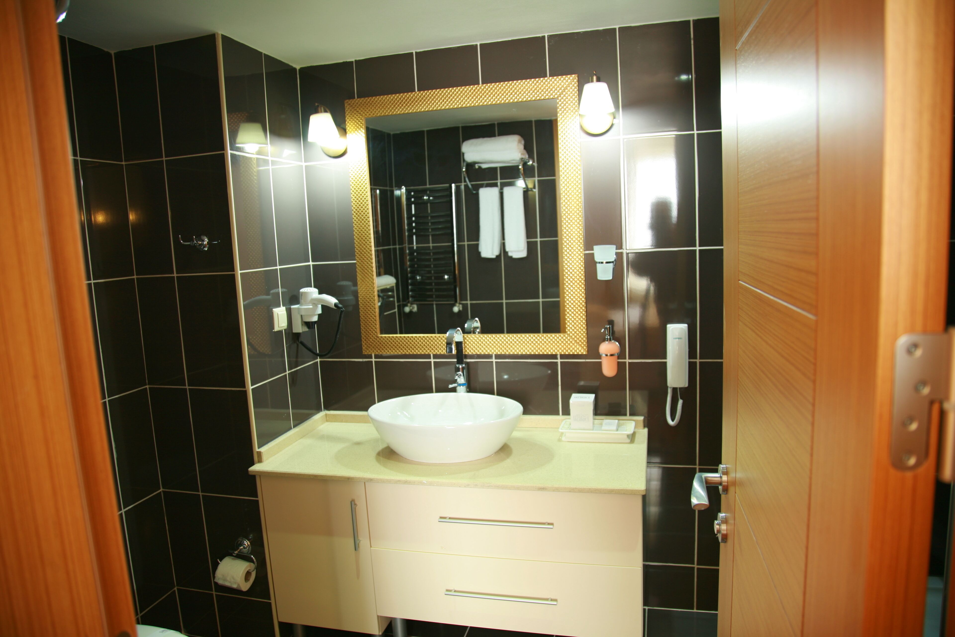 Un baño con un lavamanos blanco, un espejo con marco dorado y un perchero para toallas.