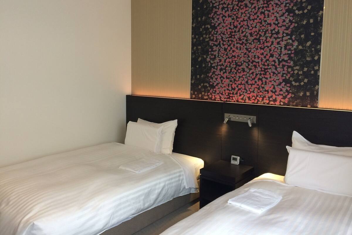 Een hotelkamer met twee enkele bedden, een nachtkastje met een klok en een groot abstract schilderij aan de muur.