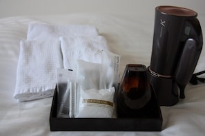 Een hotelkamer met een keurig gevouwen witte handdoek, een douchemuts en een zwarte haardroger op een dienblad.