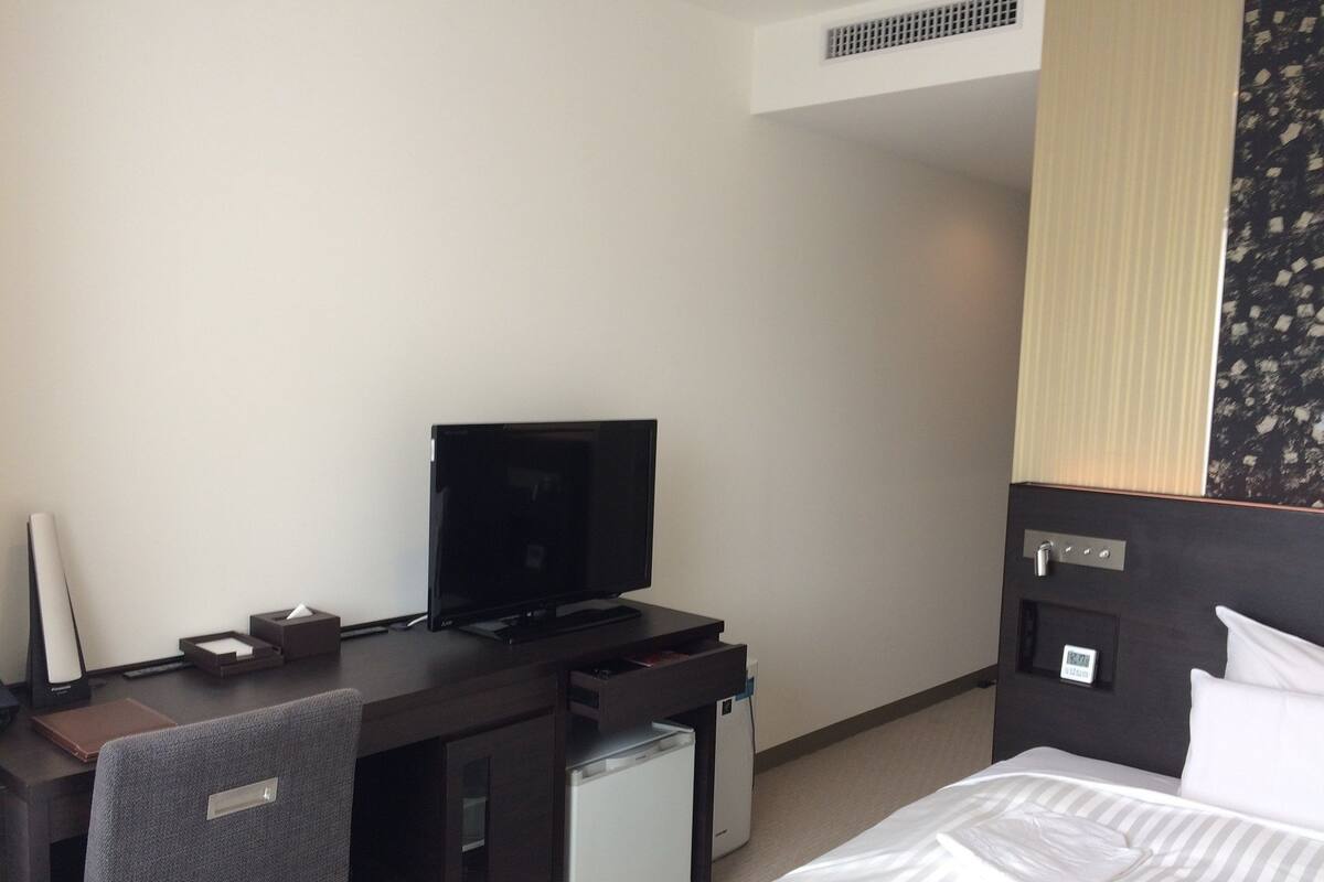 Een hotelkamer met een bed, een bureau met een televisie, een kleine koelkast en een stoel.